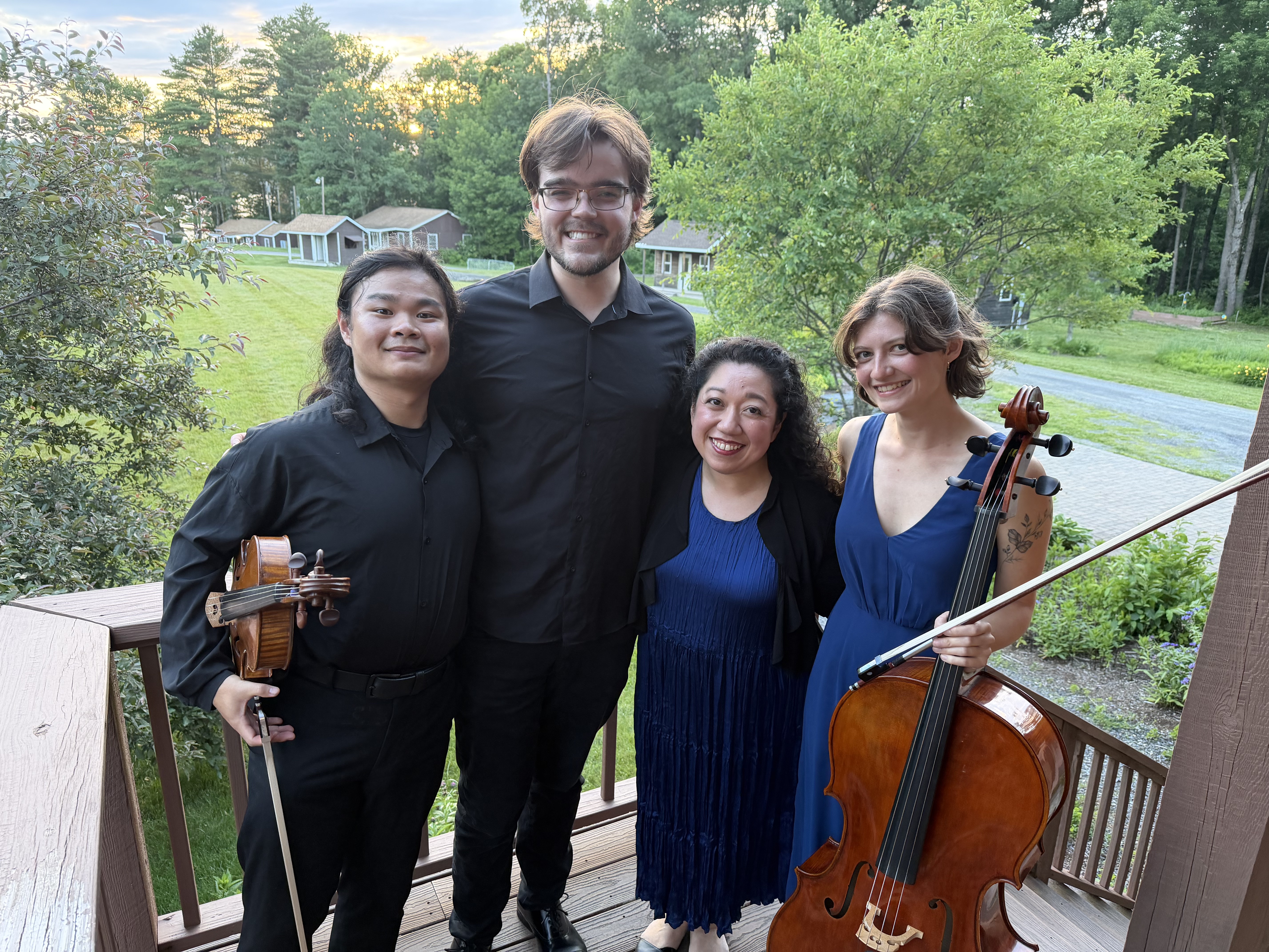 Kuang and fellow musicians with their instruments, outdoors among trees.