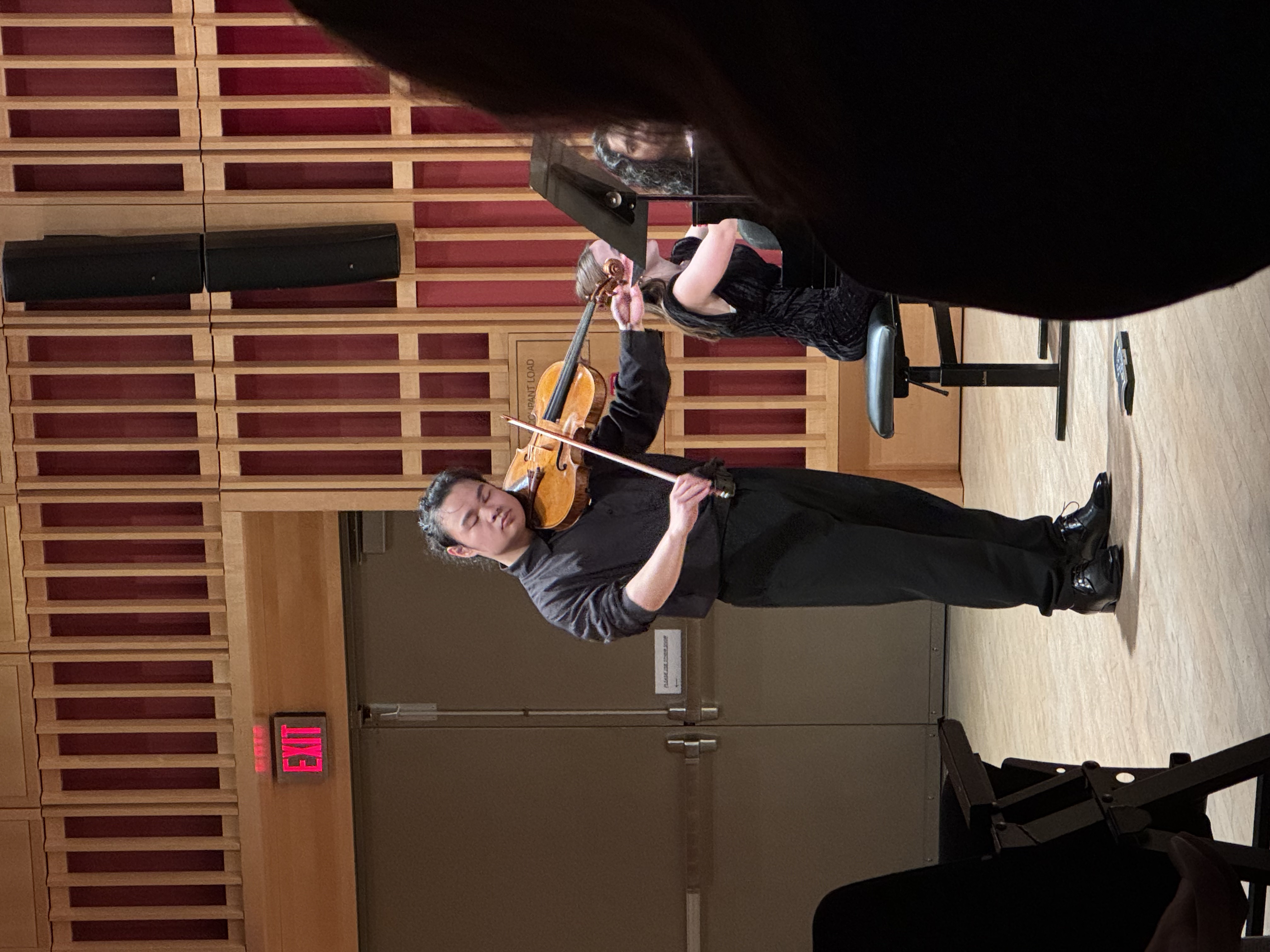 A viola performance with a pianist in a wooden concert hall.